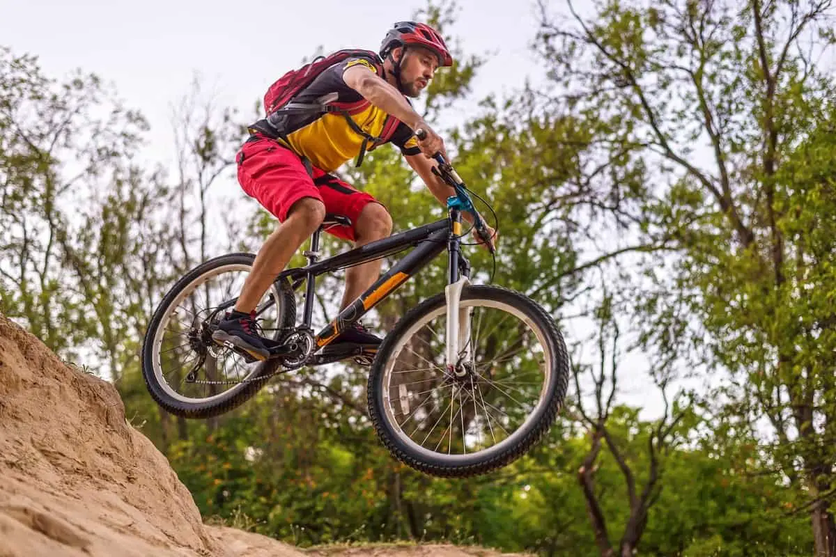 mountain bike rider wearing red and black helmet airborne after going over small jump