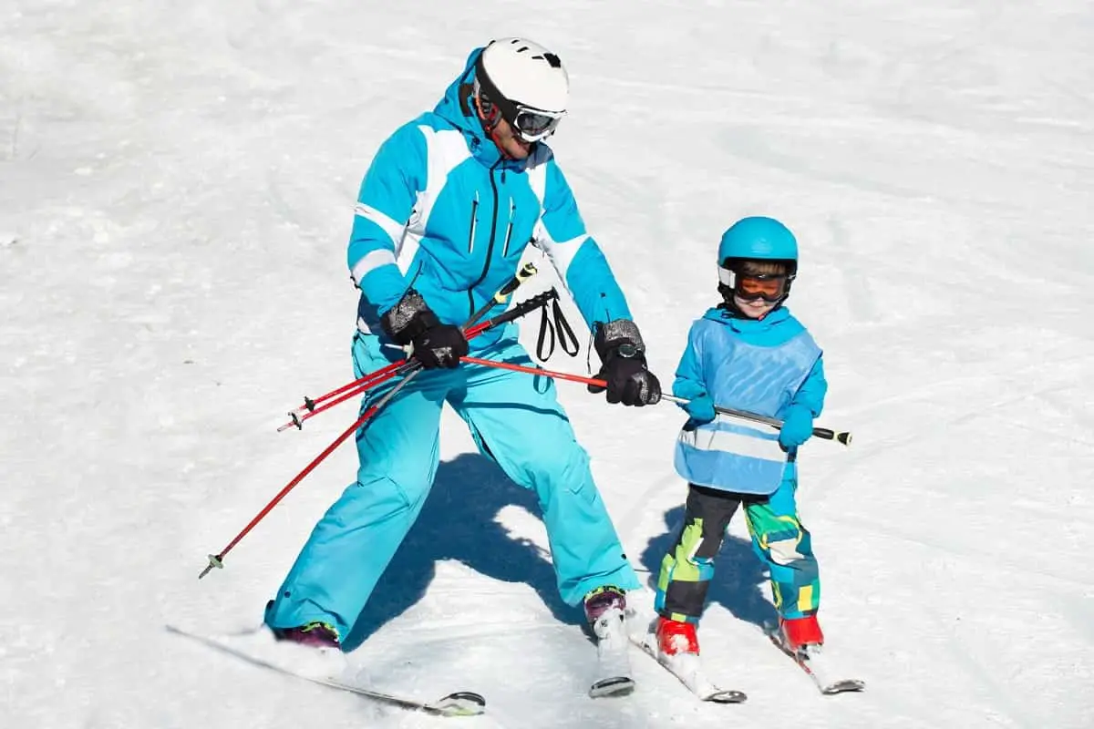 adult teaching young child how to snow ski