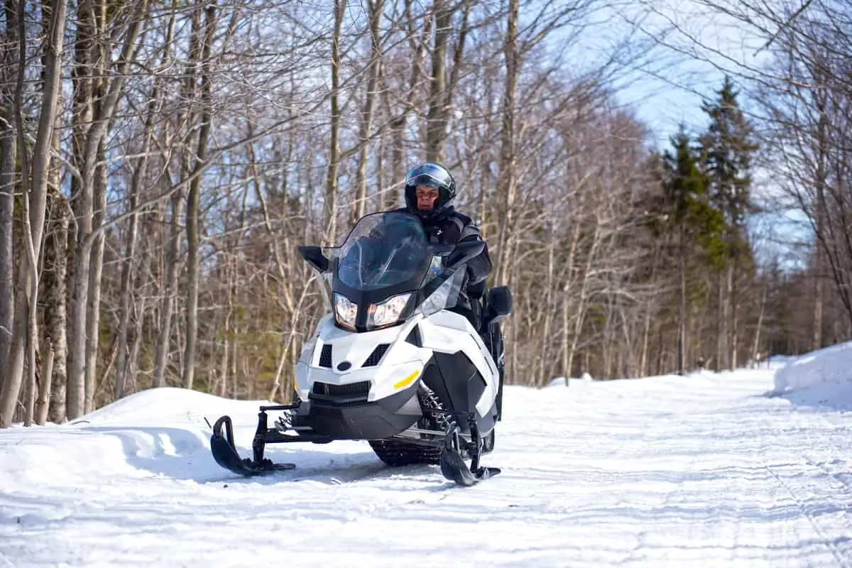 older man driving snowmobile along tree lined track on sunny day