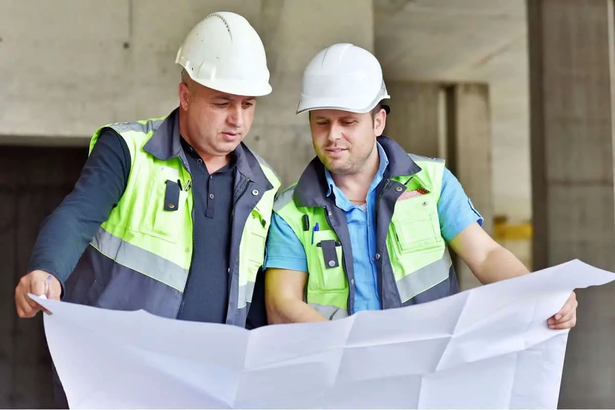 two civil engineers wearing white hard hats looking at large paper plan