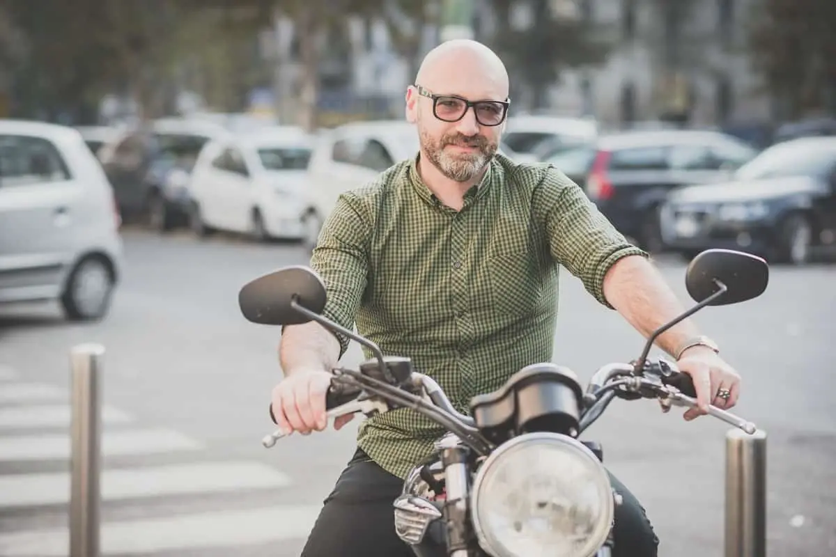 bald-headed man wearing glasses sitting on motorcycle without a helmet