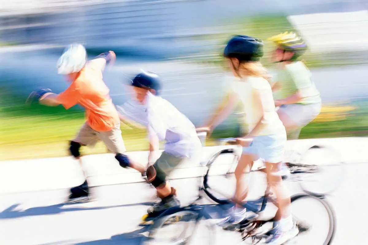 two kids on bikes and two on skates wearing helmets racing each other