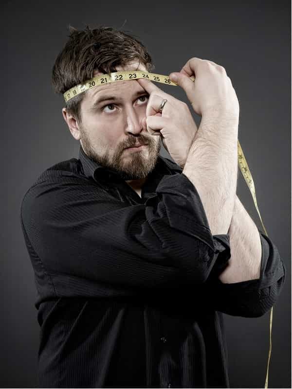 man with beard wearing a black shirt measuring his head circumference with a yellow tape measure