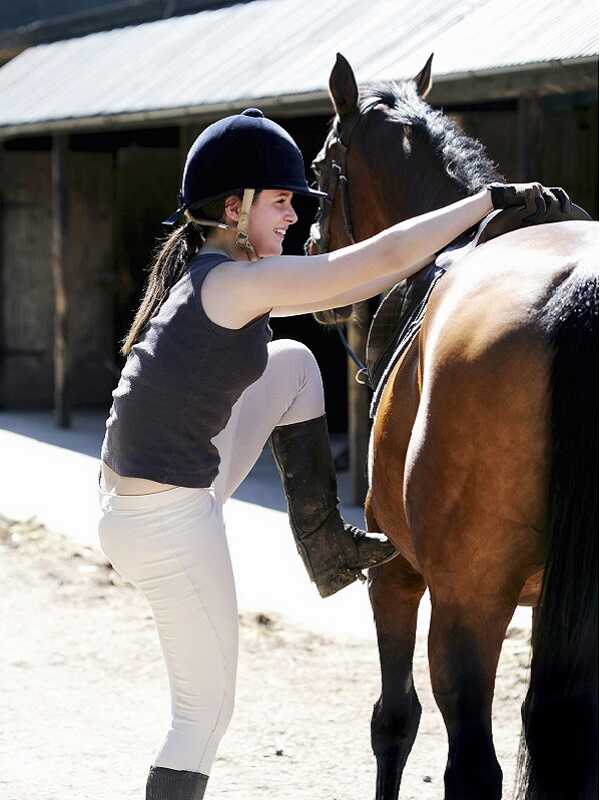 teenage girl with foot in stirrup about to mount a horse