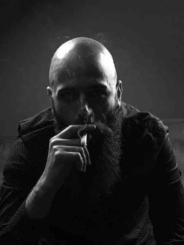 black and white image of bald headed man with long black beard smoking a cigarette