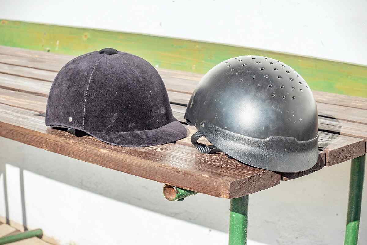 two different horse riding helmets sitting on a wooden bench