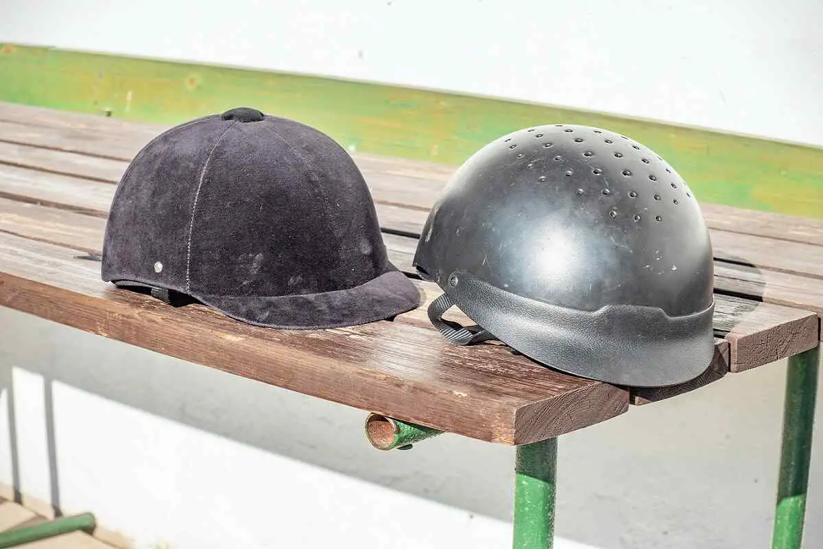 What Are Horse Riding Helmets Made Of? 1 two different horse riding helmets sitting on a wooden bench