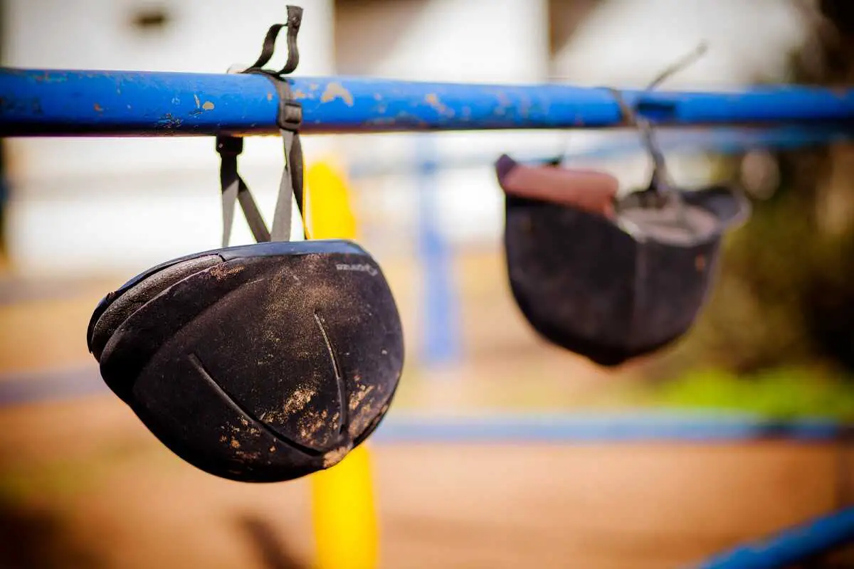 two old horse riding helmets hanging on a blue metal bar