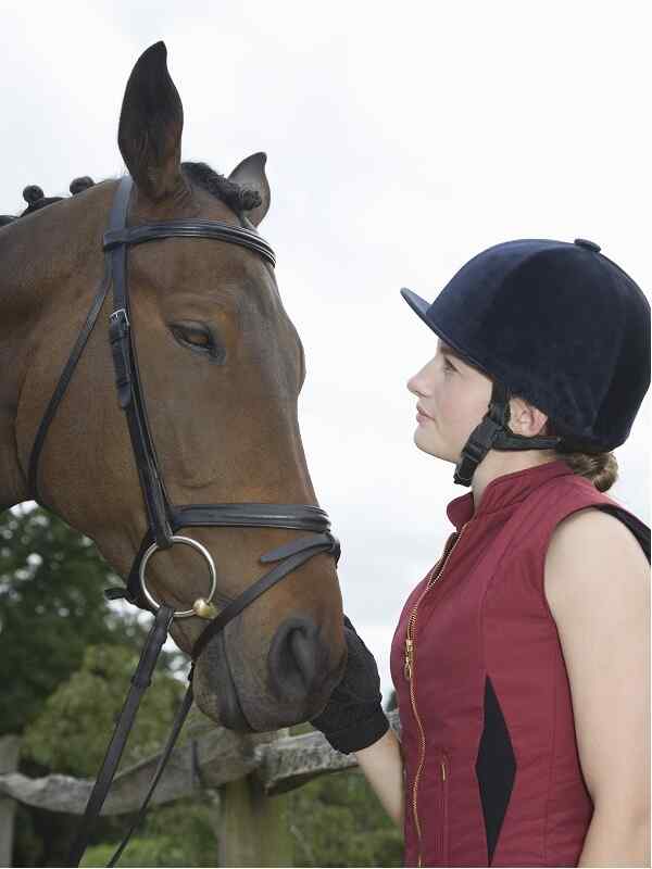 brown horse and woman wearing black riding helmet face to face