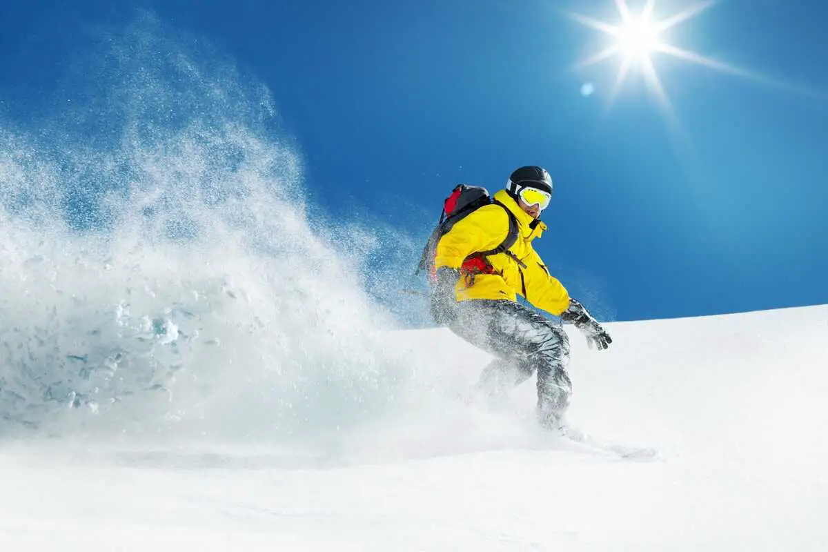 Snowboarder wearing his snowboard helmet with Bluetooth coming fast down a hill with the sun shining behind him.