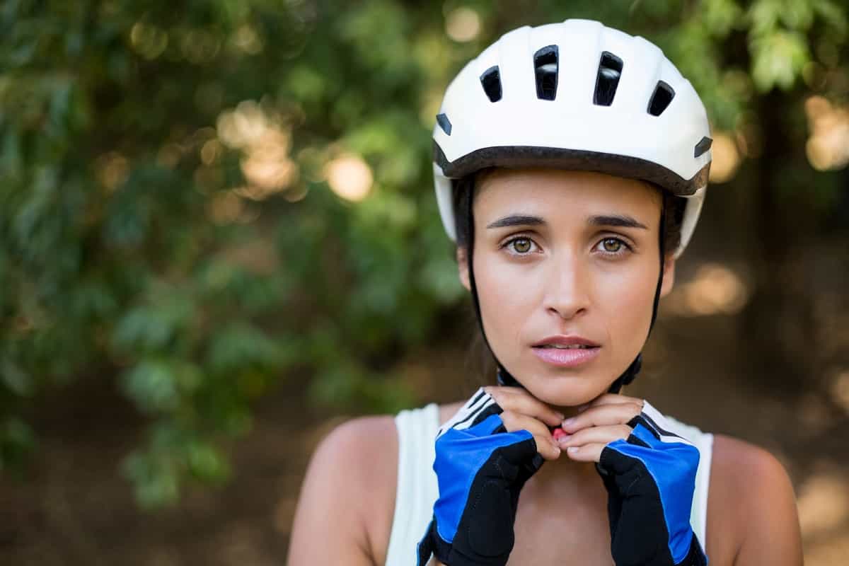 young woman fastening chin strap on white bicycle helmet