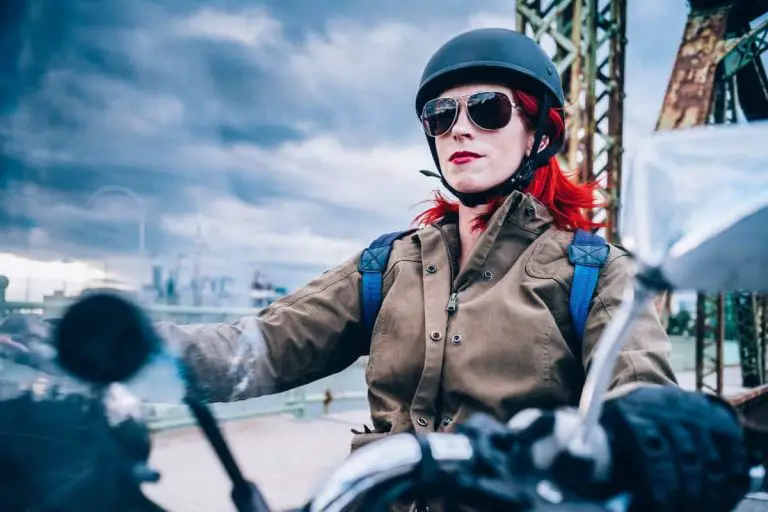 Woman with red hair wearing a half helmet riding a motorcycle.