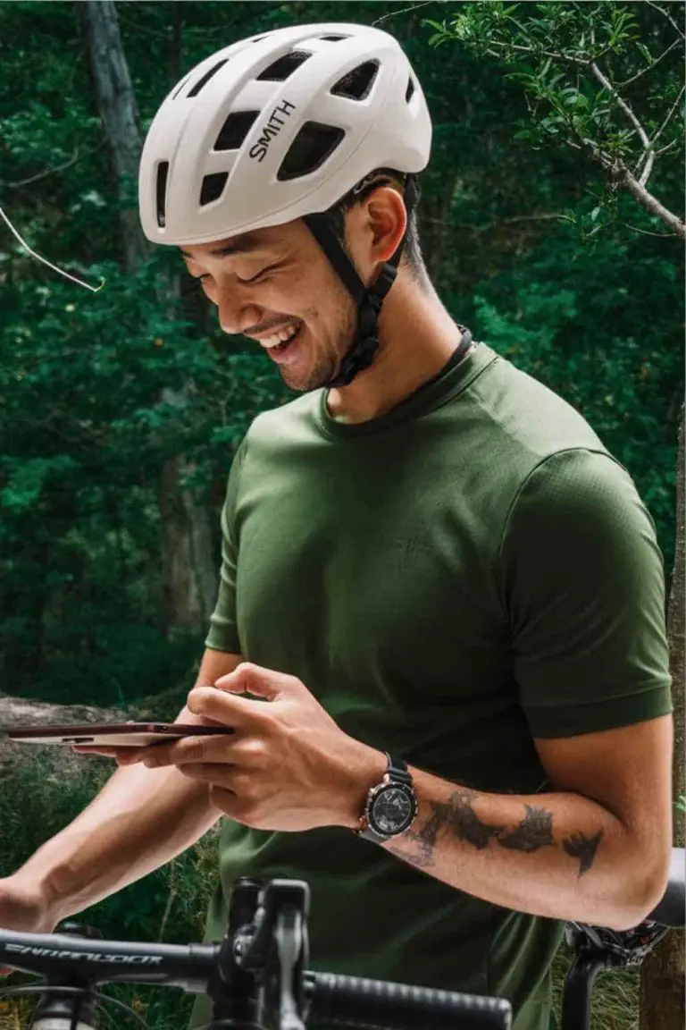 Asian man wearing a Smith Triad bike helmet in a forest setting. He is looking at his smart phone.
