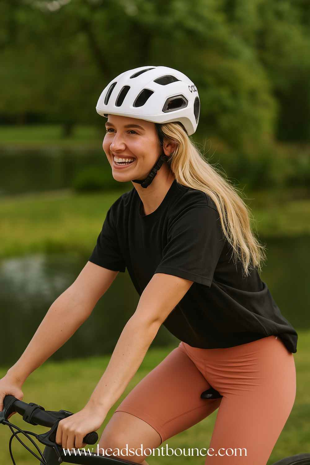 Close-up of a happy cyclist wearing a a black t-shirt and a POC Ventral road bike helmet cycling in a park with a small lake and trees in the background.