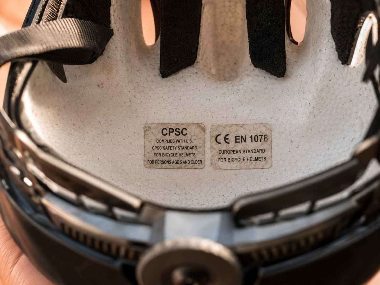 Close-up inside a bicycle helmet showing CPSC and CE EN 1078 certification stickers on white EPS foam.