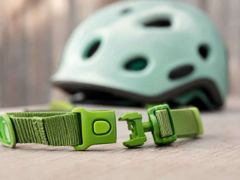 Bright green children’s bicycle helmet chin strap buckle shown partially open in front of a softly blurred pastel helmet.