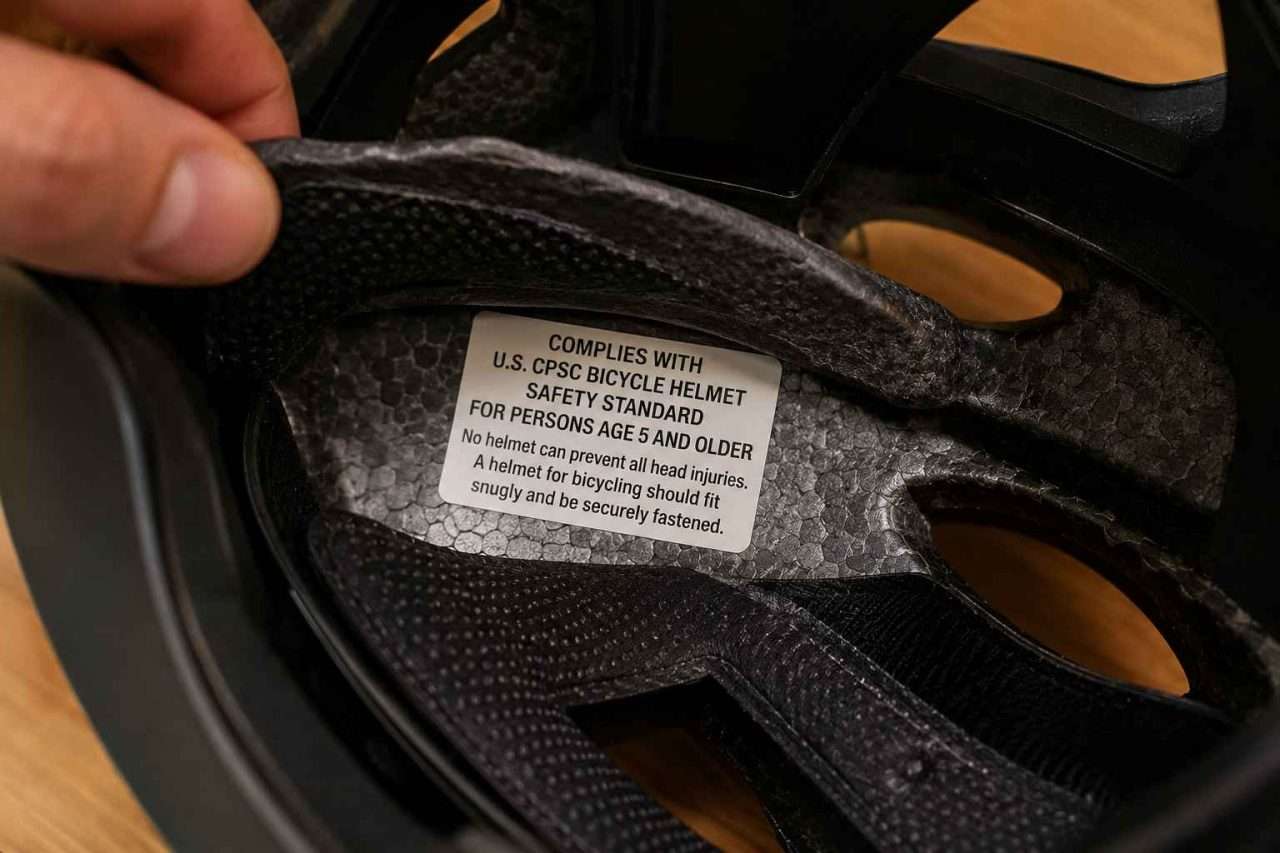 Close-up of a bicycle helmet interior with padding lifted to reveal a CPSC certification label for persons age 5 and older.