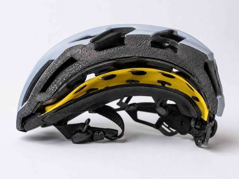 Cross-section of a modern bicycle helmet showing the outer shell, EPS foam liner, yellow MIPS slip-plane, and comfort padding.