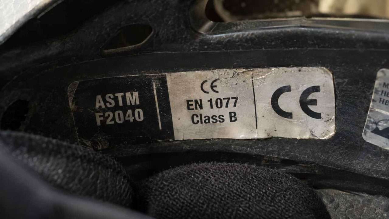 Close-up of a ski helmet interior label showing ASTM F2040, CE EN 1077 Class B, and CE certification markings.