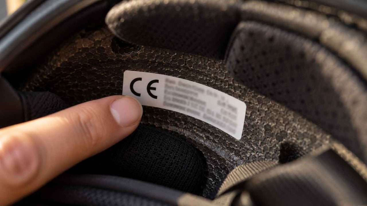 Fingertip pointing to a white label with a visible CE mark inside a helmet.